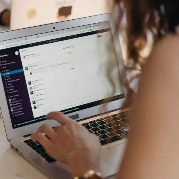 A businesswoman typing on a laptop in an office setting, using Slack for communication.